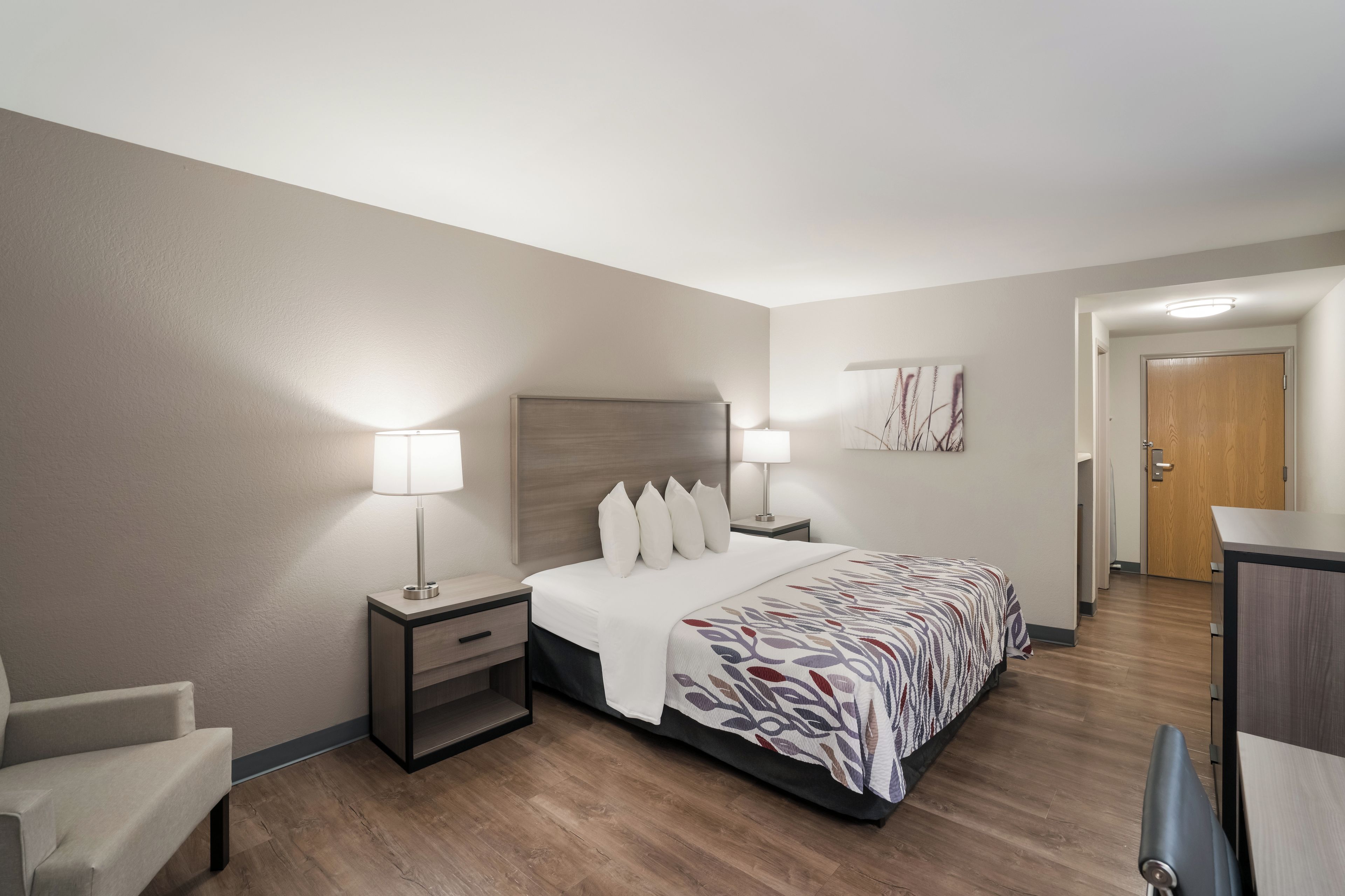 Une chambre d’hôtel avec un lit, des tables de chevet, une chaise, un bureau et une porte.