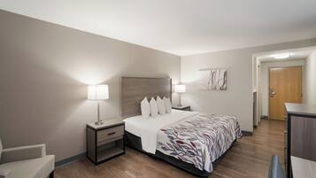 Une chambre d’hôtel avec un lit, des tables de chevet, une chaise, un bureau et une porte.