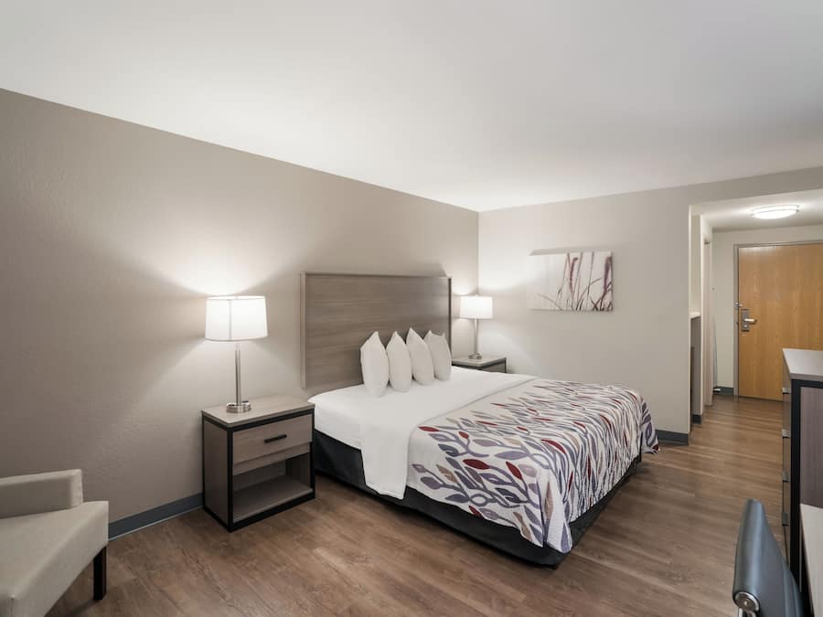 Une chambre d’hôtel avec un lit, des tables de chevet, une chaise, un bureau et une porte.