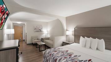 Ein Hotelzimmer mit Bett, Schreibtisch, Sessel, Sofa und einem an der Wand befestigten Fernseher.