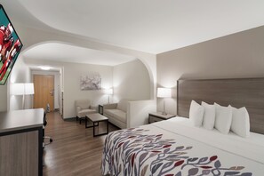 Une chambre d’hôtel équipée d’un lit, d’un bureau, d’une chaise, d’un canapé et d’un téléviseur fixé au mur.