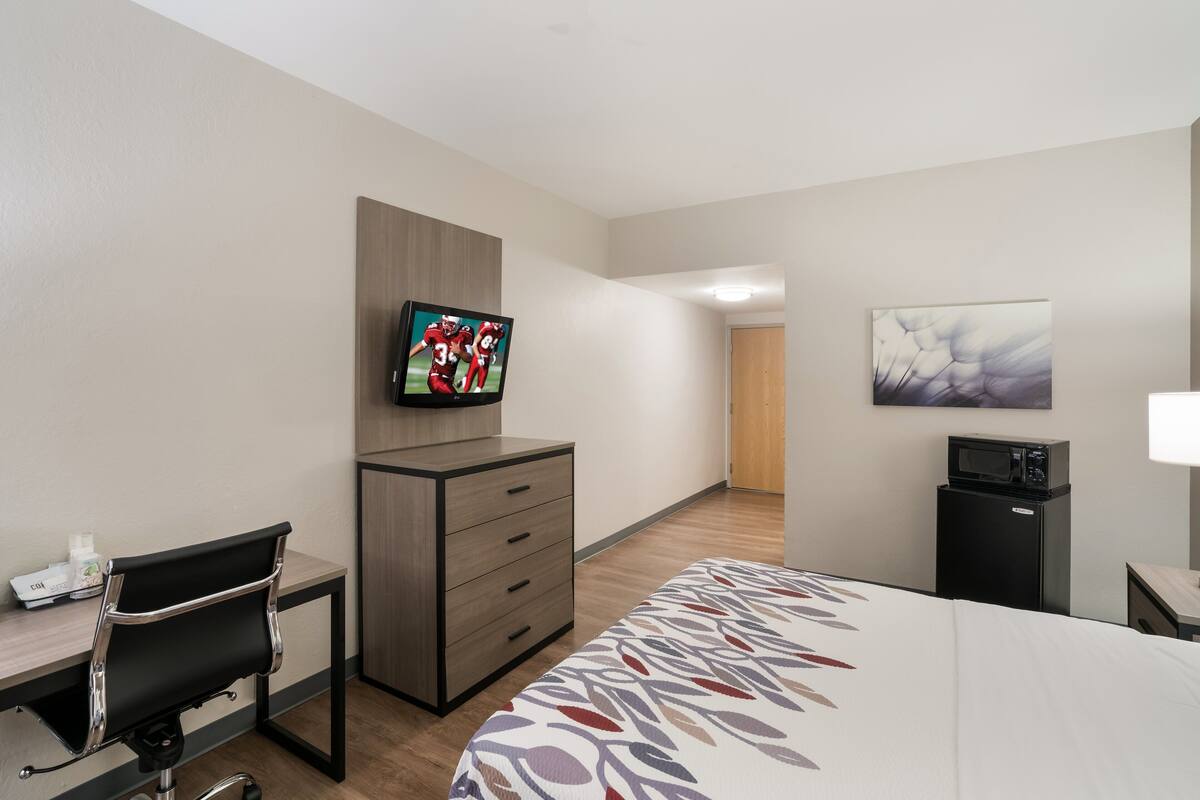 A hotel room with a bed, a desk with a chair, a television, a microwave, and a small cabinet.