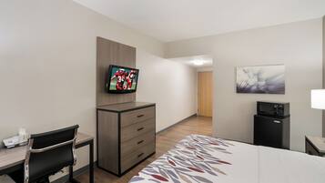 A hotel room with a bed, a desk with a chair, a television, a microwave, and a door leading to another room.
