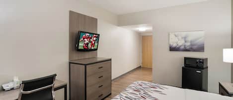 Habitación de hotel con cama, escritorio con silla, televisor, microondas y puerta que da a otra habitación.