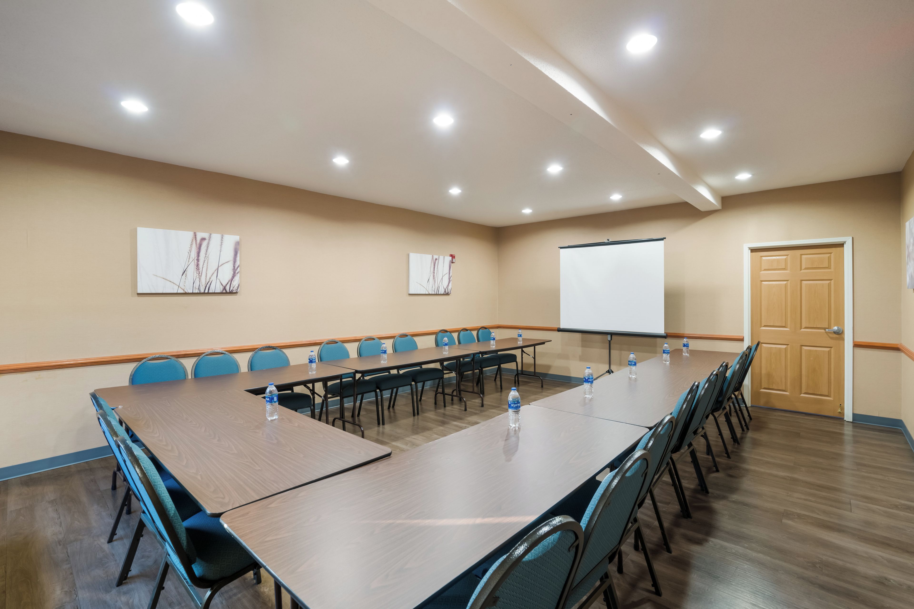 Un salón de conferencias con una larga mesa, sillas, una pizarra y dos cuadros en la pared.