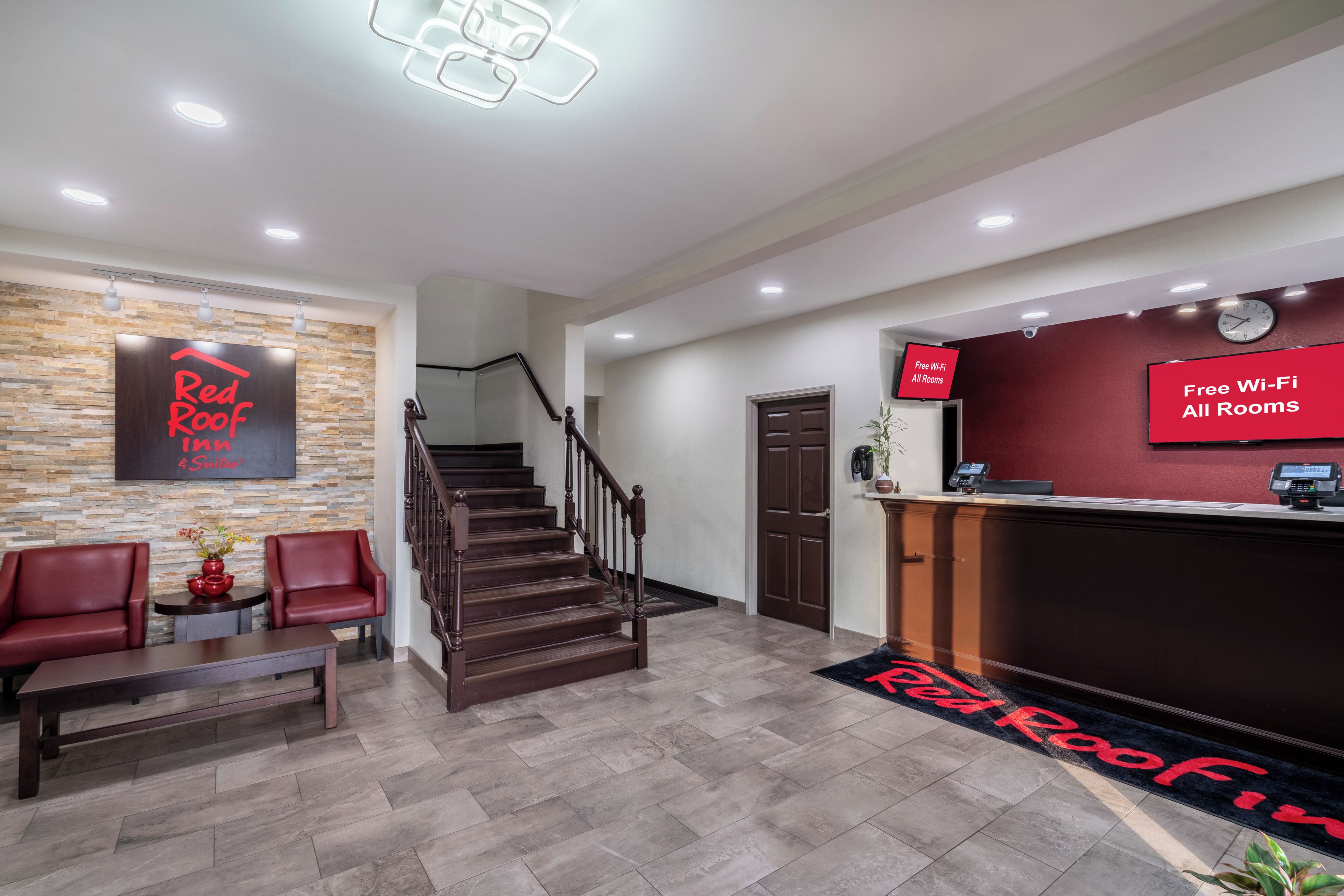 Un espace d’accueil d’hôtel comprenant un escalier, des sièges et un écran numérique indiquant la disponibilité du Wi-Fi gratuit.