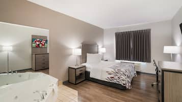Een hotelkamer met een bed, nachtlampjes, een televisie, een badkamer met bad en een groot raam met gordijnen.