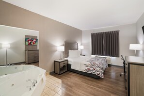 Quarto de hotel com cama, luminárias de cabeceira, televisão, banheiro com banheira e uma grande janela com cortinas.