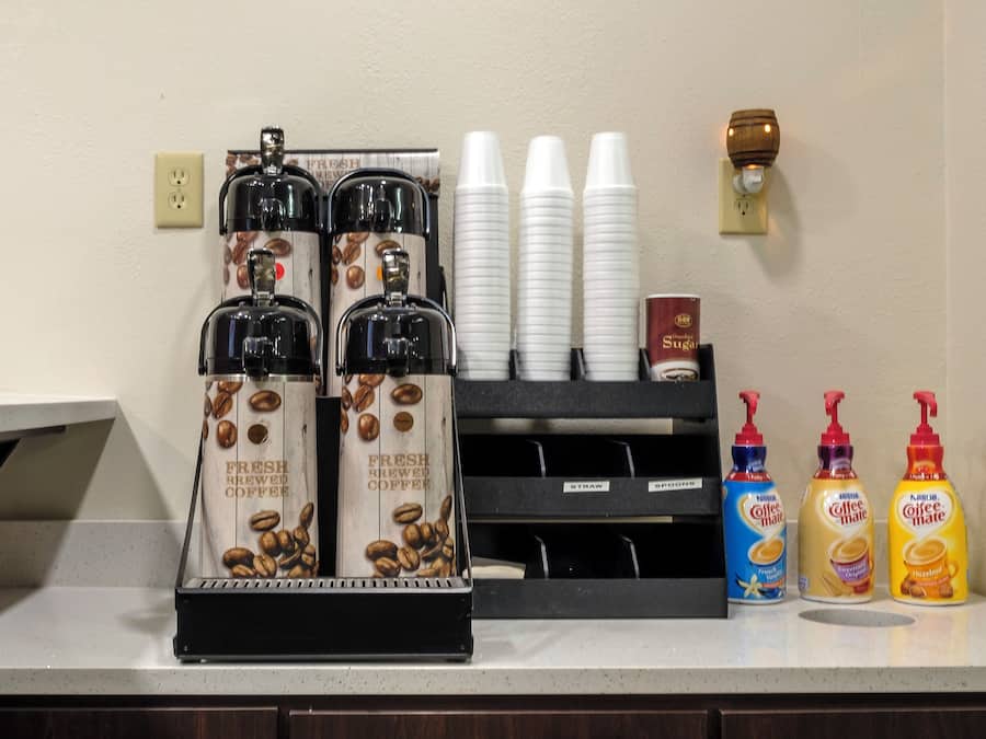 A coffee station with coffee dispensers, cups, and coffee creamer bottles.