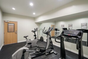 Uma academia com equipamentos de exercícios, um espelho e uma porta.