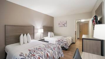 Ein Hotelzimmer mit zwei Betten, einem Schreibtisch, einem Stuhl, einer Lampe und einem Fernseher.