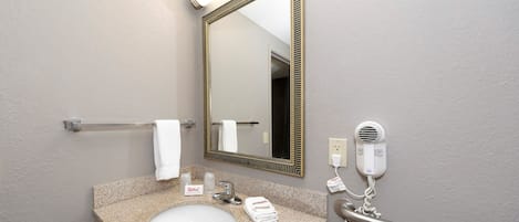 A bathroom with a granite sink, a mirror with a gold frame, a towel rack, a hand dryer, and a red towel dispenser.