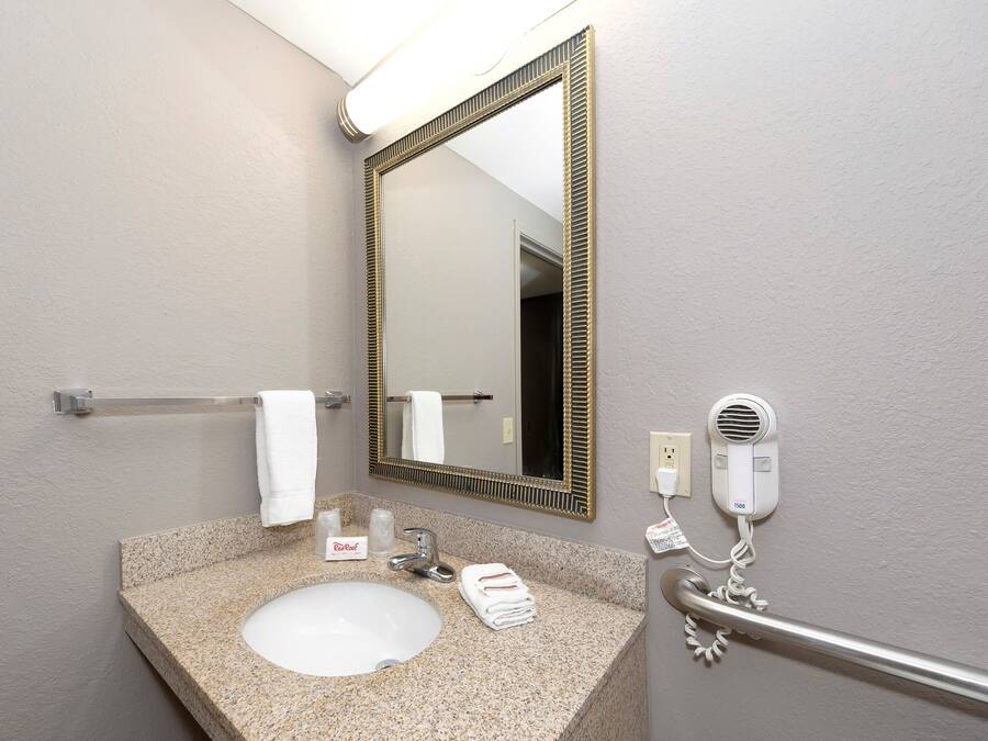 Un baño con lavamanos de granito, un espejo con marco dorado, toallero, secador de manos y dispensador de toallas rojo.