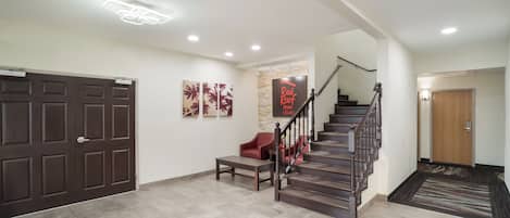 A spacious foyer with a wooden staircase, a bench, and a wall-mounted sign for Red Roof Inn & Suites.
