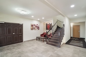 A spacious foyer with a wooden staircase, a bench, and a wall-mounted sign for Red Roof Inn & Suites. - Red Roof Inn & Suites Carrollton, GA–West Georgia (Carrollton)