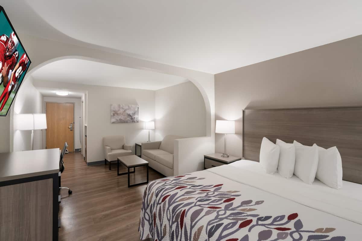 A hotel room with a large bed, a desk, a chair, a sofa, and a TV mounted on the wall.
