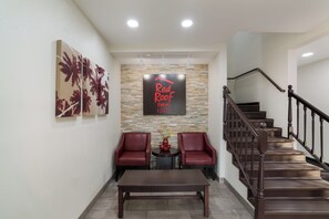 Un área de recepción con una escalera, dos sillones de cuero rojo, una mesa de madera y un cartel en la pared.