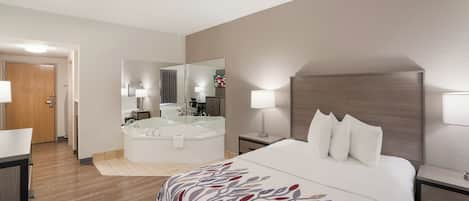 A hotel room with a large bed, a bathroom with a bathtub, and a desk with a chair.