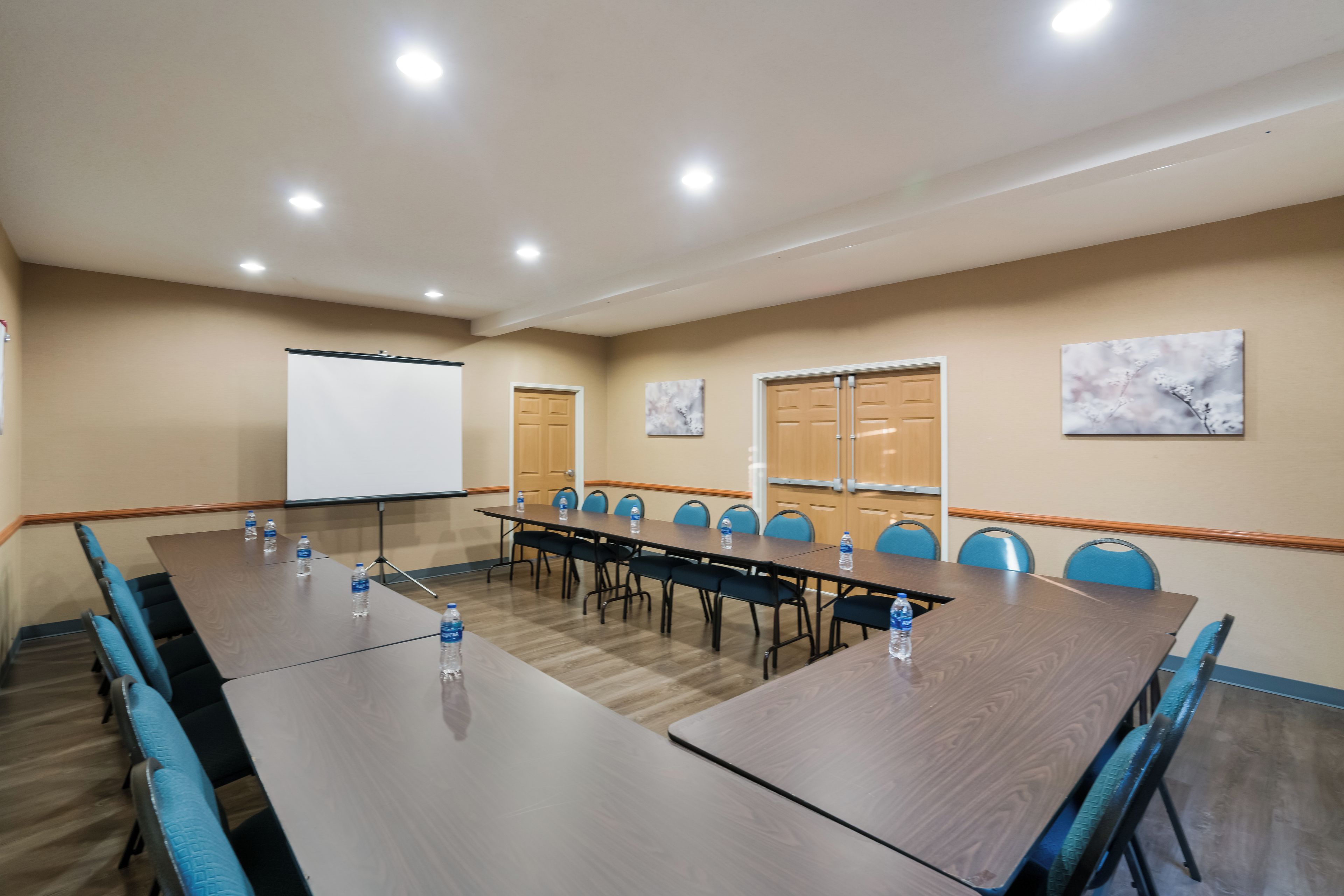 Une salle de conférence avec une longue table, des chaises, un écran de projection et deux portes.