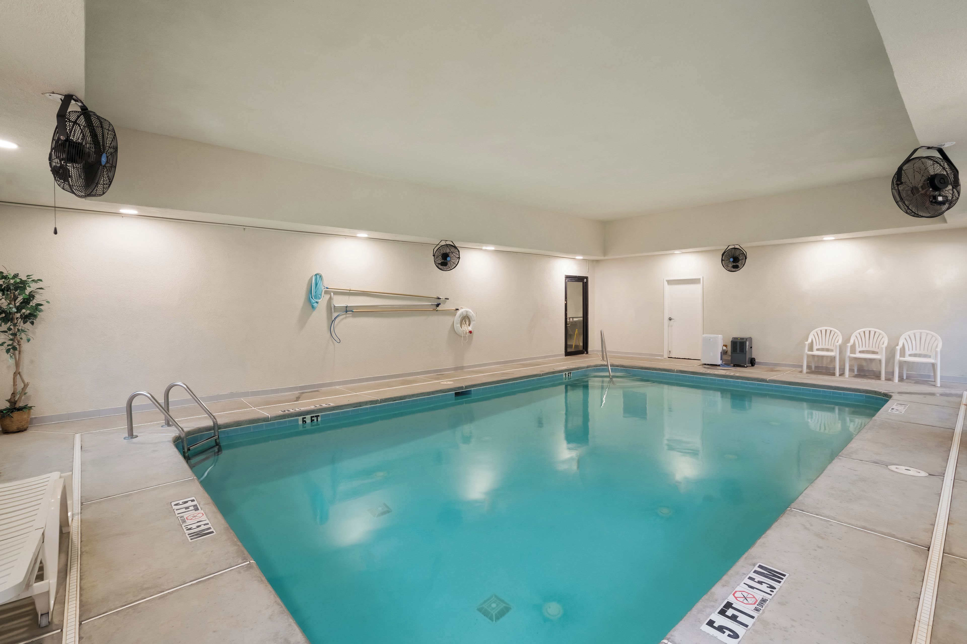 Una piscina interior con agua cristalina, un trampolín y un ventilador de techo.