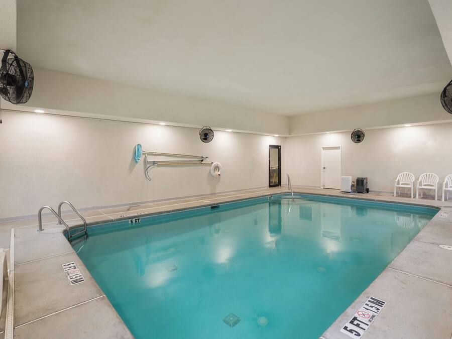 An indoor swimming pool with clear water, a diving board, and a ceiling fan.