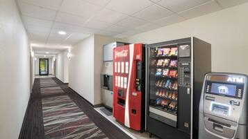 Pasillo de hotel con máquinas expendedoras, incluyendo un refrigerador de Coca-Cola, una máquina de aperitivos y un cajero automático.