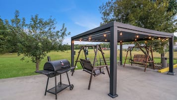 An outdoor patio with a grill, swing set, and string lights.