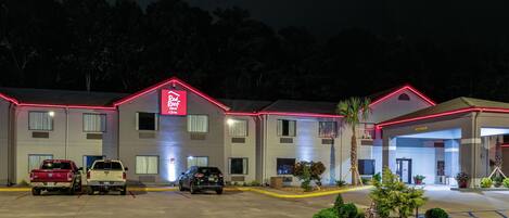 Un hôtel avec une enseigne rouge sur le toit, de nombreuses places de stationnement et une entrée bien éclairée.