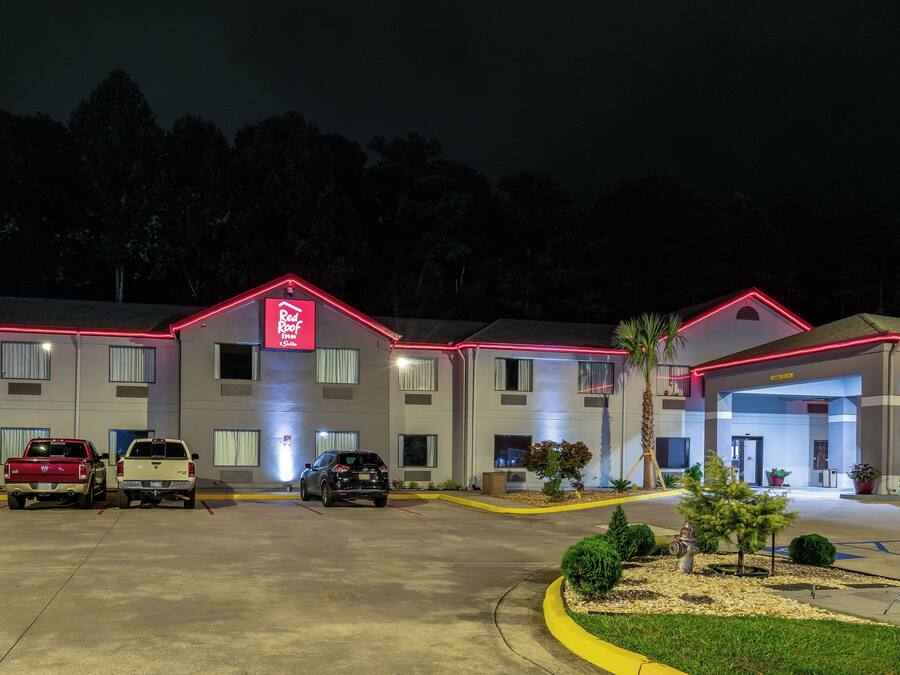 Un hotel con letrero de techo rojo, varios espacios de estacionamiento y una entrada bien iluminada.