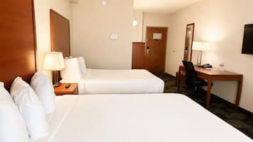 A hotel room with two beds, a desk, a chair, a lamp, a television, and a door.