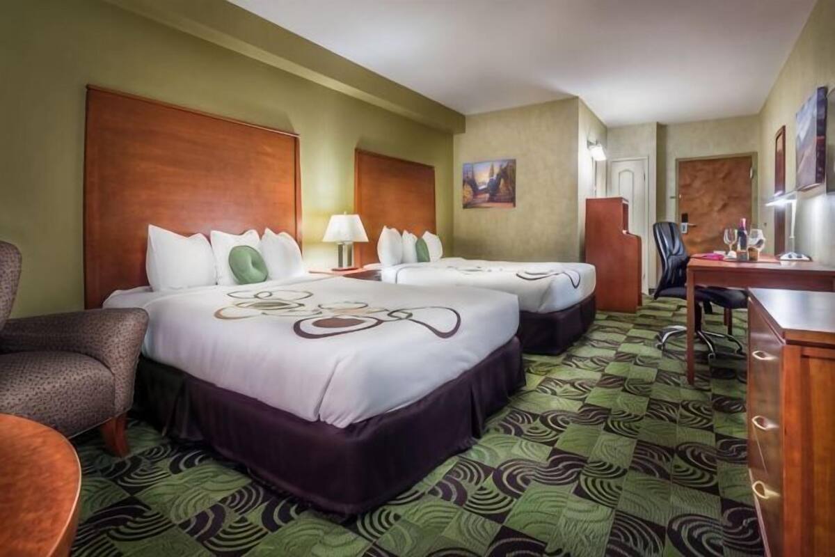 A hotel room with two beds, a desk, a chair, and a small table.