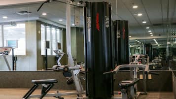 Academia com equipamentos de ginástica, espelhos e piso coberto de carpete.
