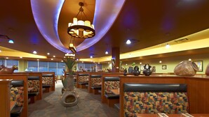 A restaurant with booths and tables, featuring patterned cushions and a central decorative vase. - Deerfoot Inn & Casino (Calgary)