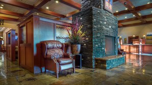 A lobby with a stone fireplace, leather armchair, and a large potted plant. - Deerfoot Inn & Casino (Calgary)