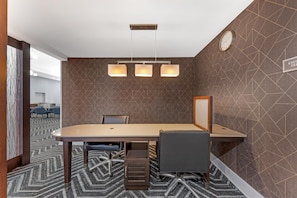 Sala de conferências com uma mesa grande, duas cadeiras, um relógio e parede com padrão geométrico.