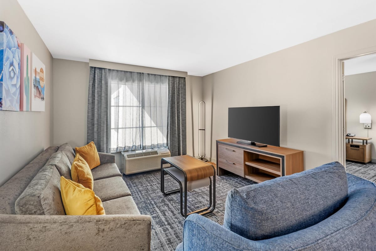 Ett hotellrum med en soffa, fåtölj, TV och ett litet träbord.