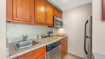 A kitchen with wooden cabinets, a stainless steel refrigerator, a microwave, a dishwasher, and a granite countertop.