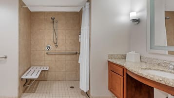 Un baño con ducha, barra de apoyo, toallero, inodoro y lavabo con espejo.