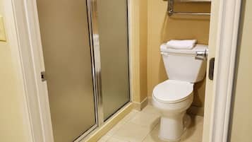 A bathroom with a toilet, a shower with frosted glass doors, and a towel rack above the toilet.
