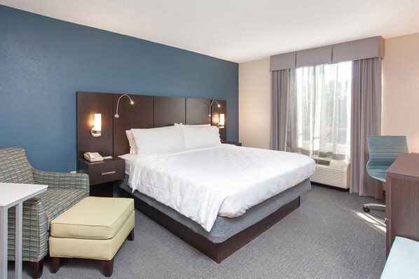 A hotel room with a bed, bedside table, lamp, chair, and a desk. - Holiday Inn Hotel & Suites Tallahassee Conference Ctr N by IHG (Tallahassee)