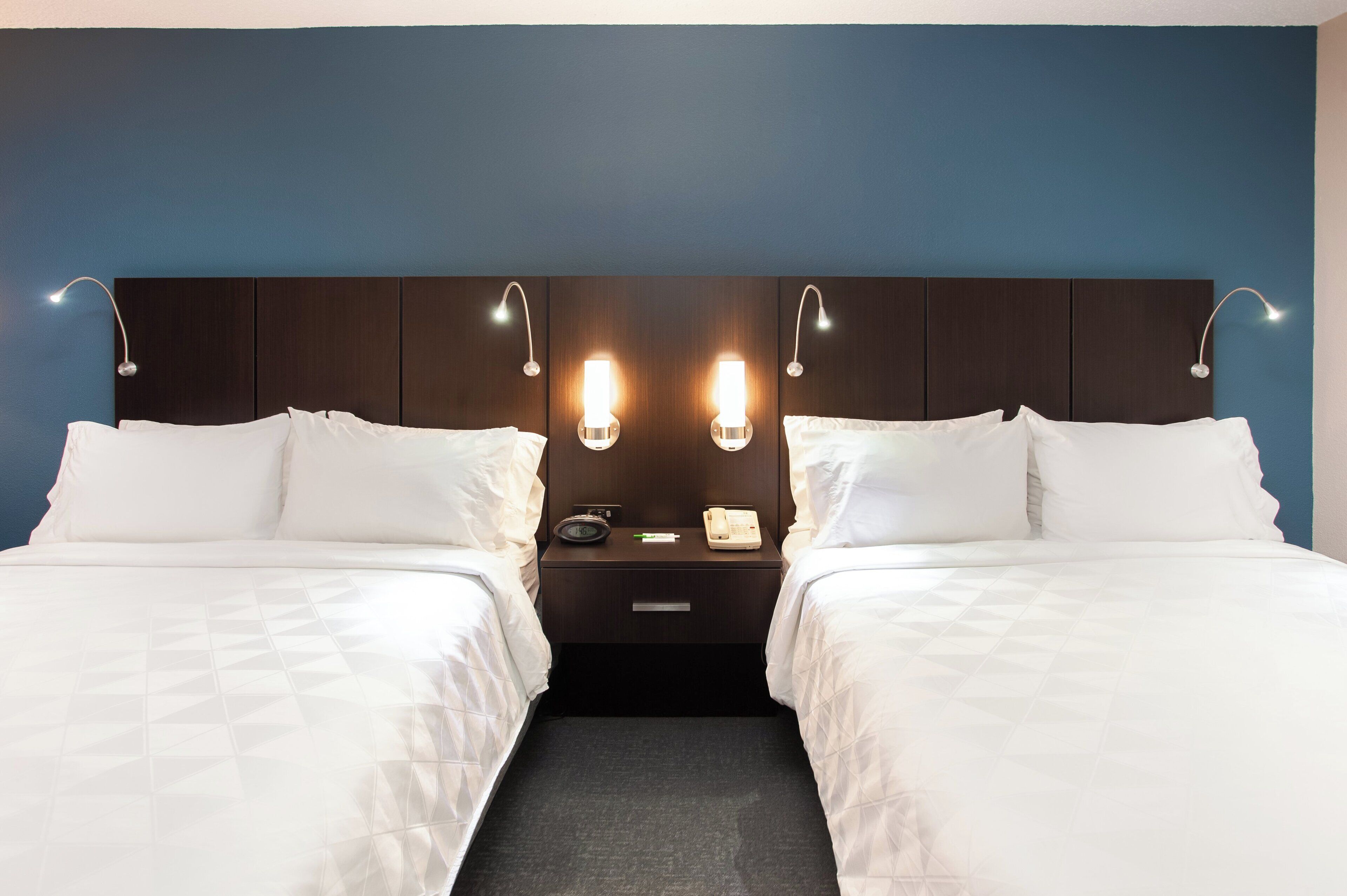 Ein Hotelzimmer mit zwei Betten, einem dunklen Kopfteil, Nachttischlampen und einem Nachttisch mit Telefon und Radio.