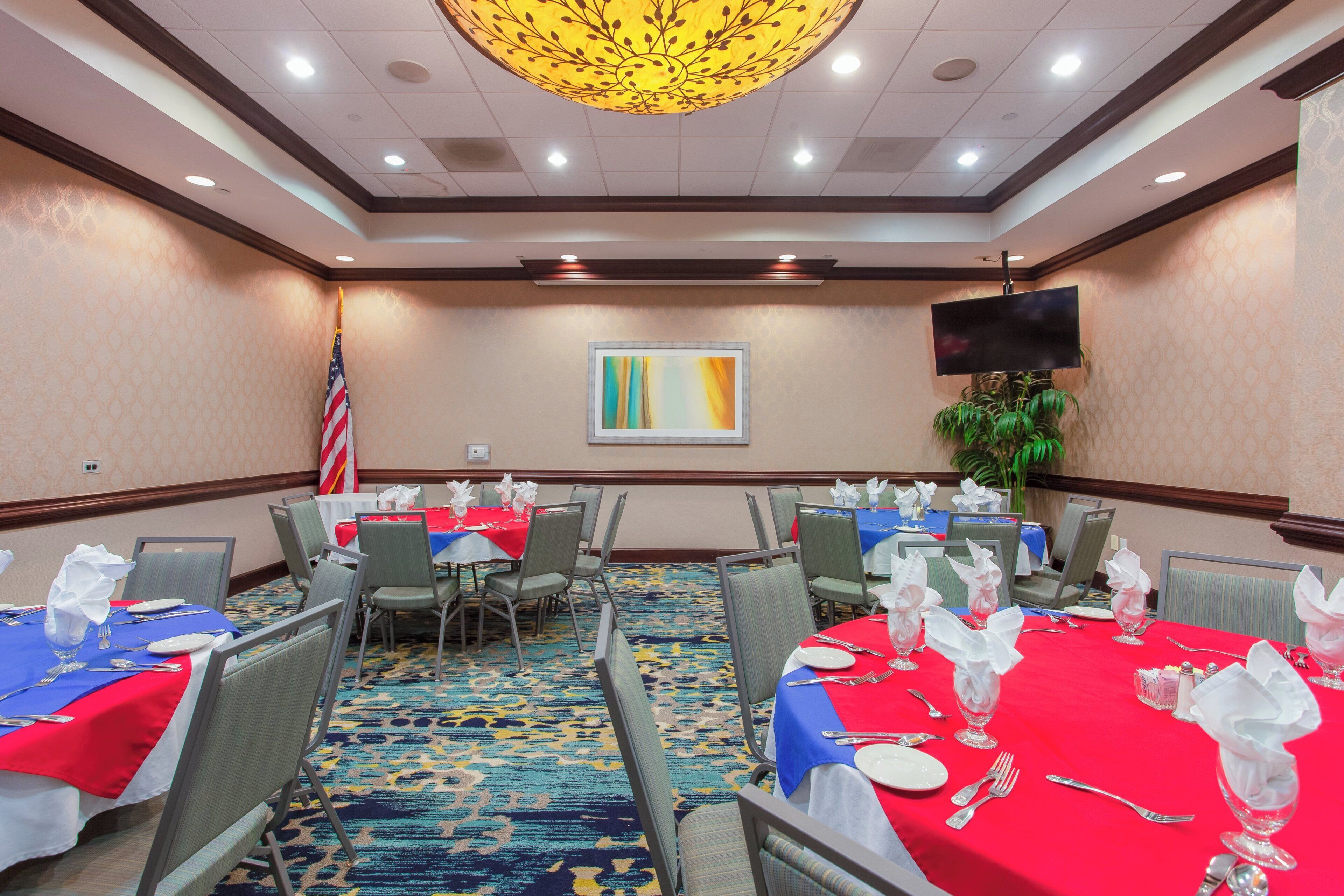 A conference room with tables set for dining, a flag, and a television on the wall.