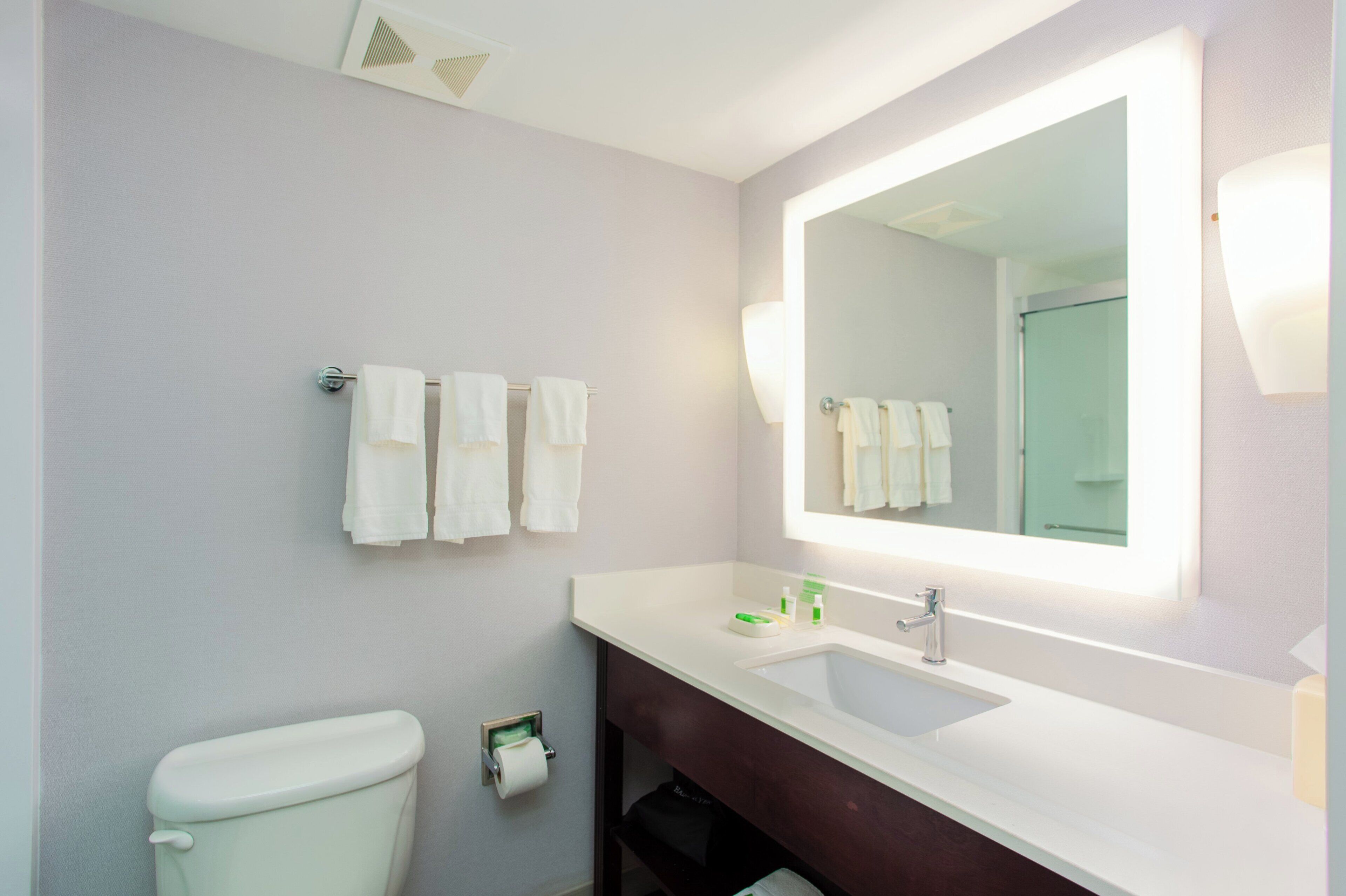 A bathroom with a toilet, a sink with a mirror, and a towel rack with multiple towels.
