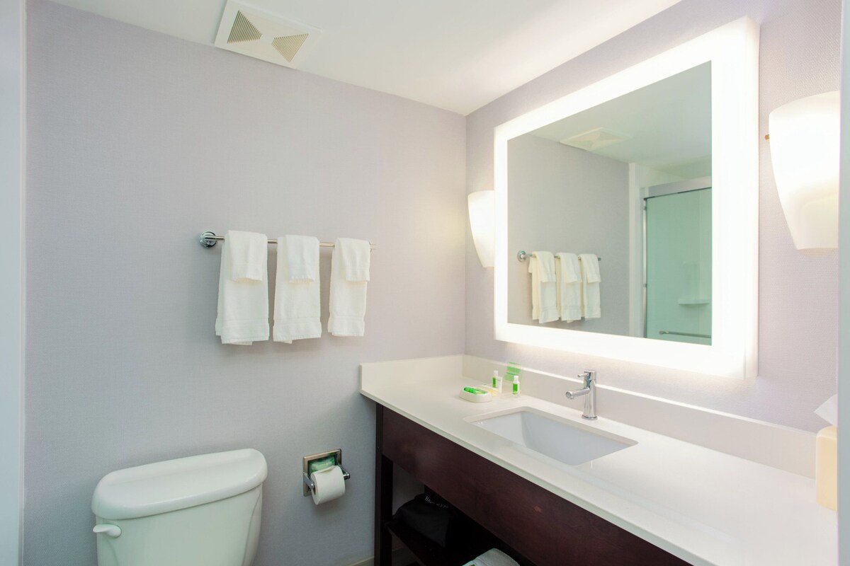 A bathroom with a toilet, a sink with a mirror, and a towel rack with multiple towels.