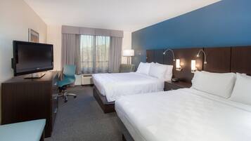 A hotel room with two beds, a desk, a chair, a television, and a window with curtains.