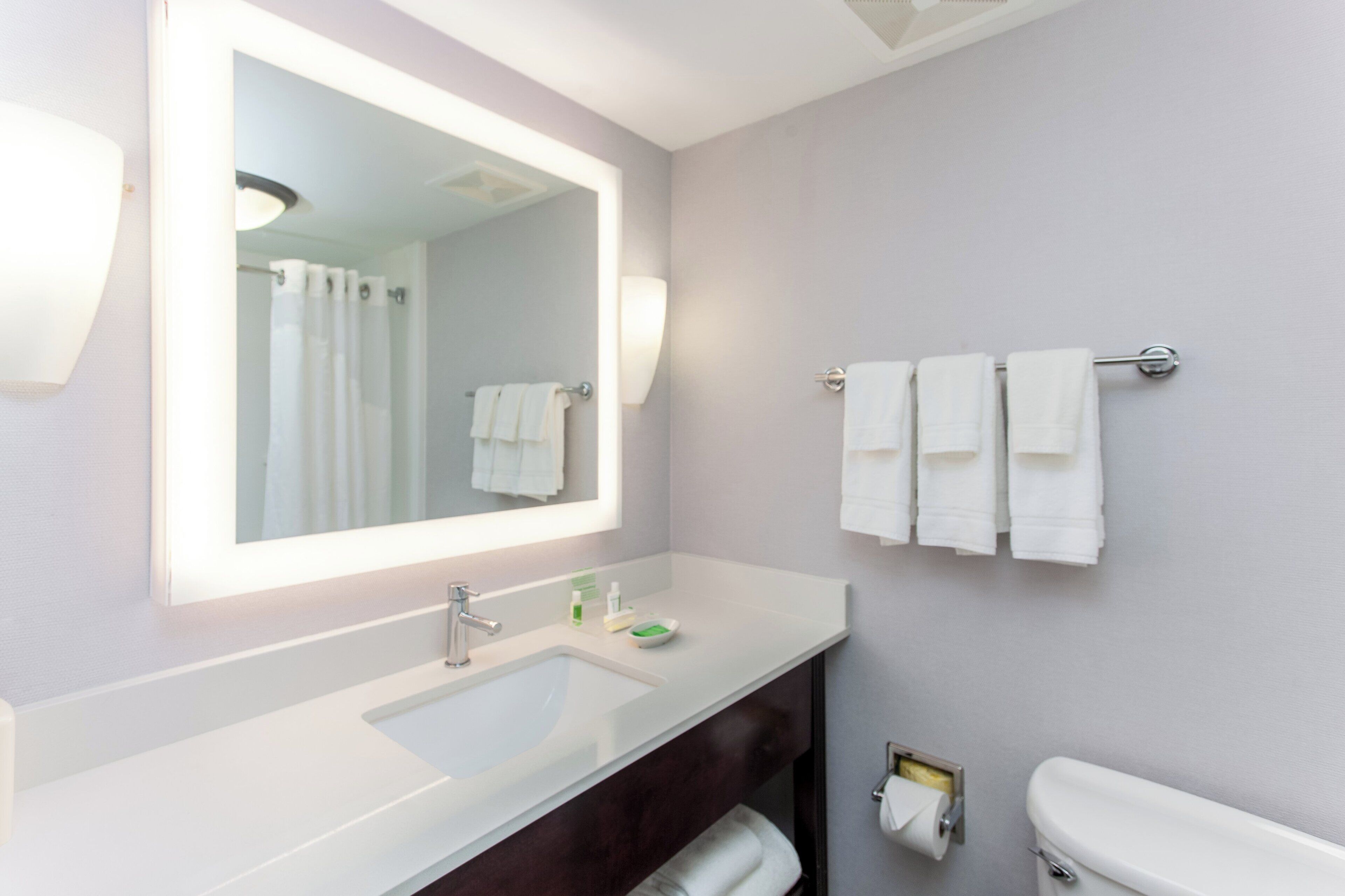 Une salle de bain moderne avec un grand miroir, un lavabo blanc et deux porte-serviettes.