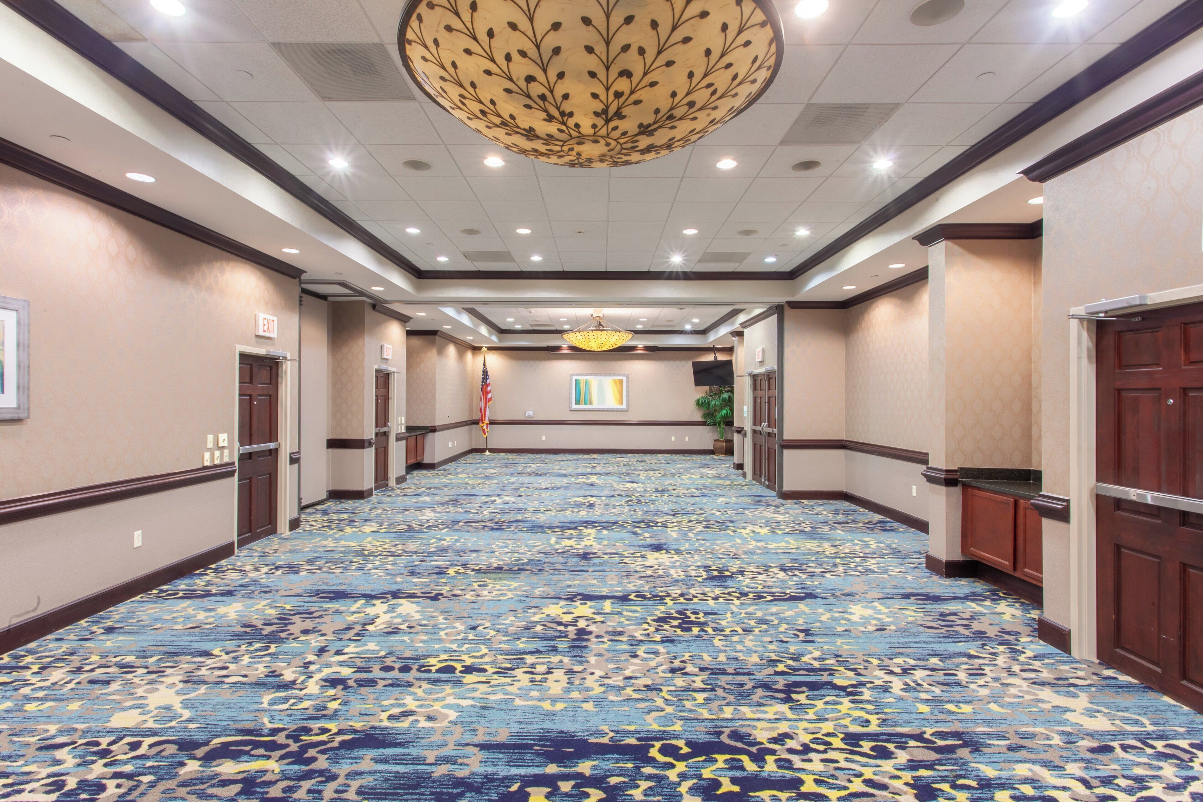 A hotel corridor with a patterned carpet, wooden doors, and a large chandelier.