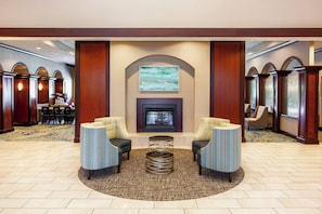 A lobby with a fireplace, two armchairs, a coffee table, and a carpeted floor. - Holiday Inn Hotel & Suites Tallahassee Conference Ctr N by IHG (Tallahassee)