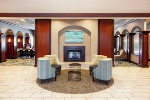 Un hall con chimenea, dos sillones, una mesa de centro y suelo alfombrado.
