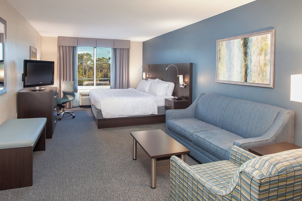 A hotel room with a bed, a sofa, a TV, a desk, and a chair.